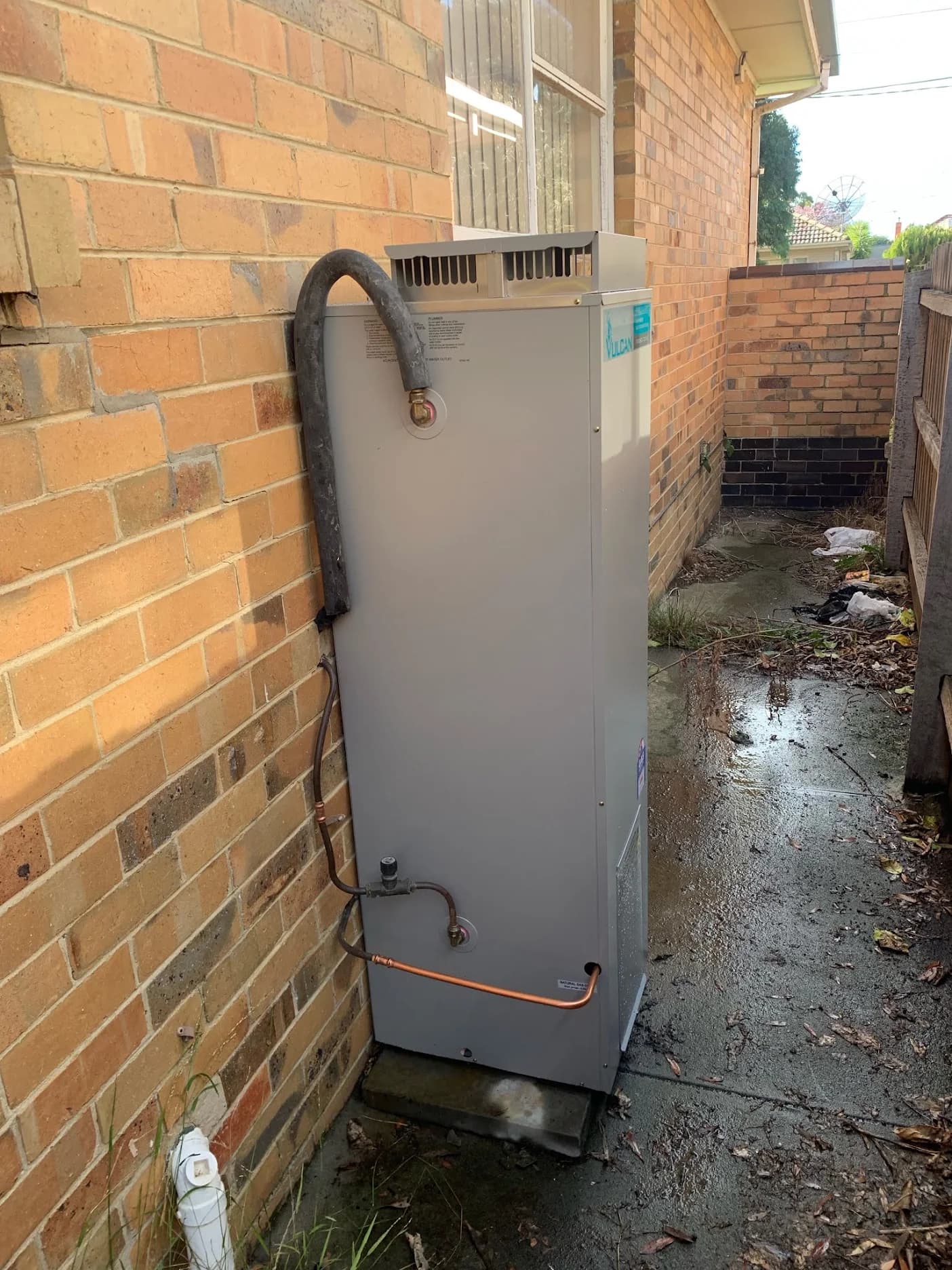 Vulcan outdoor hot water unit in a narrow brick side passage with copper pipework