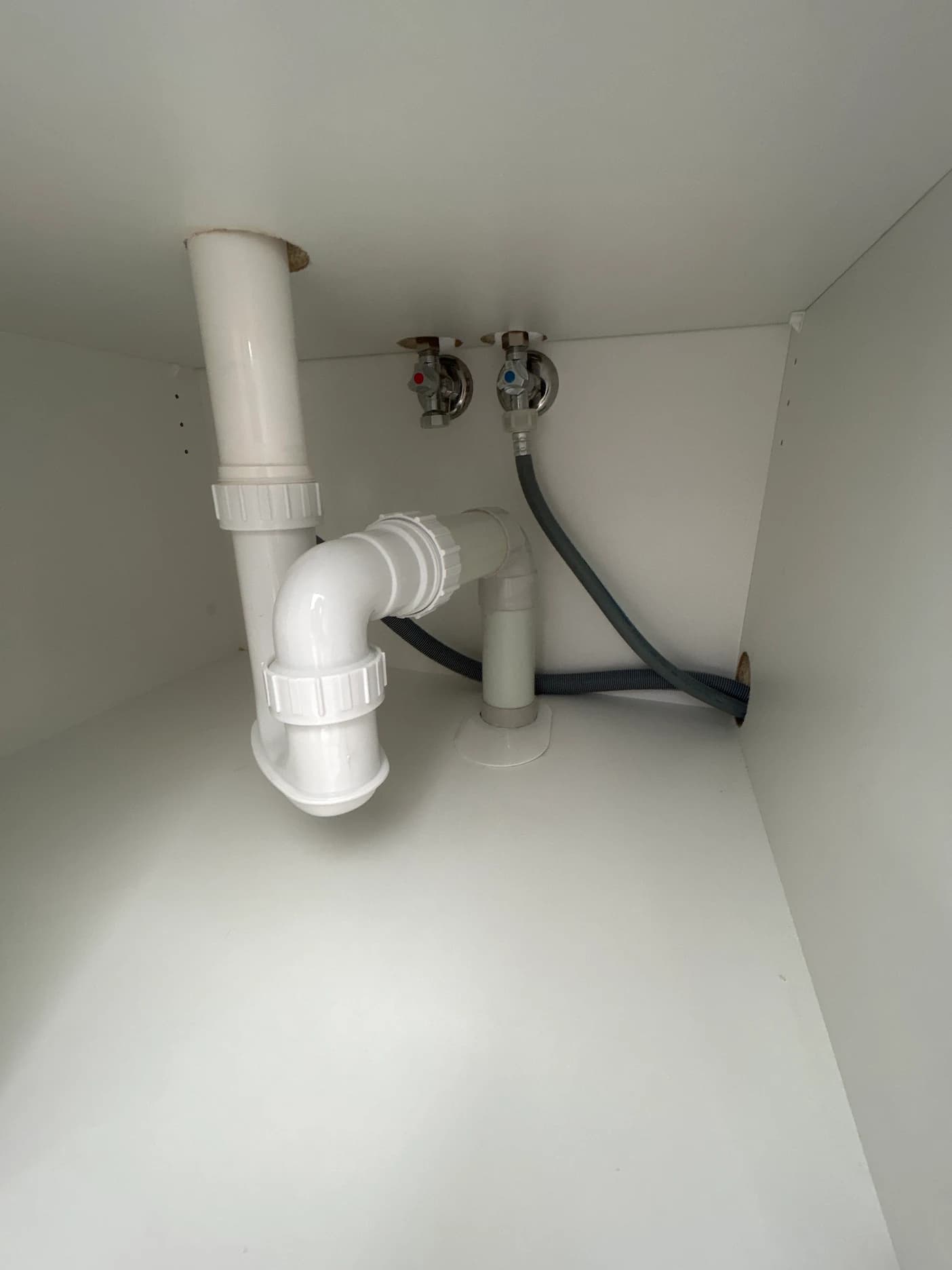 Under-sink plumbing with white PVC trap, waste pipe, and hot and cold isolation valves