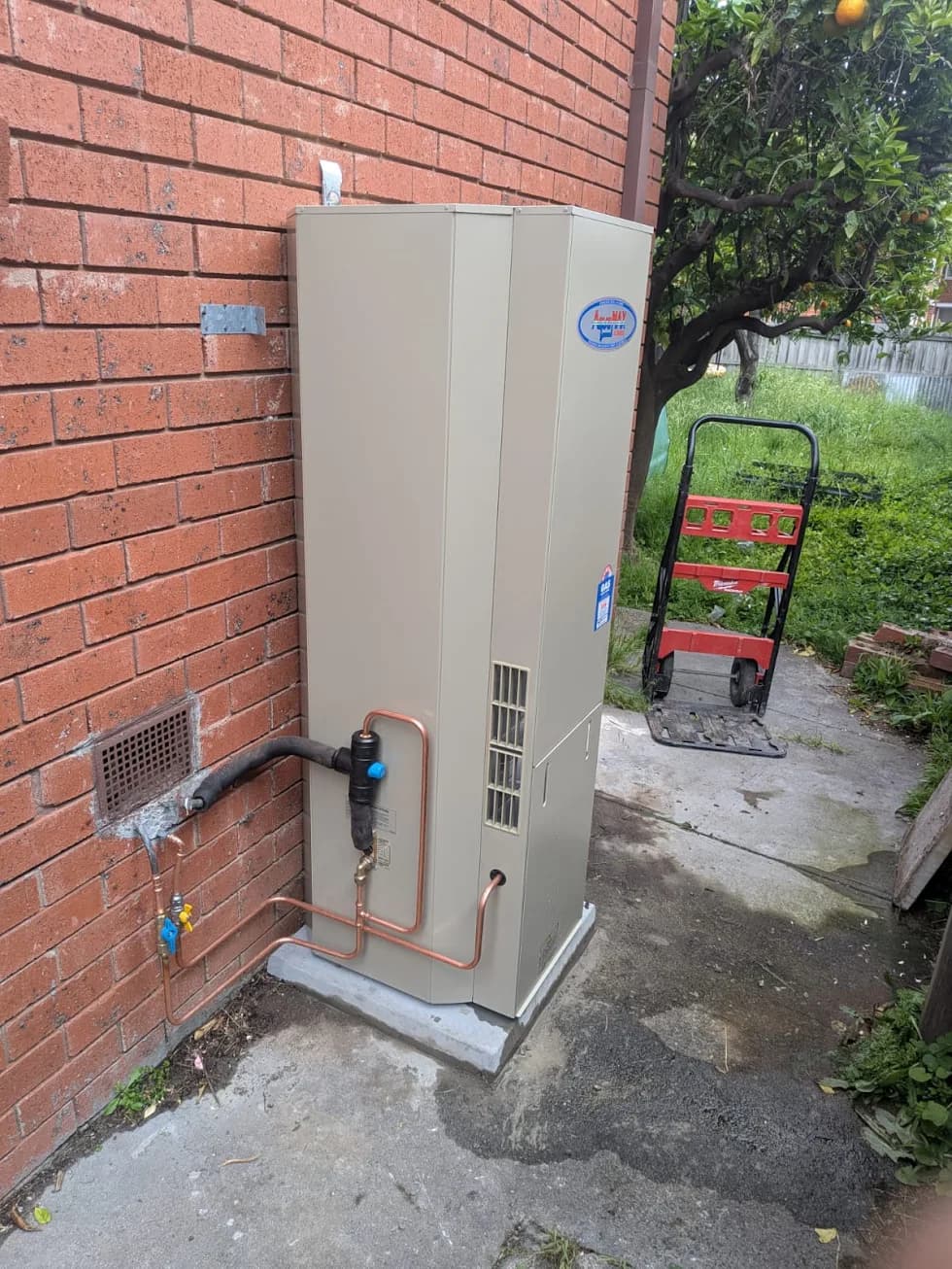Large outdoor hot water system installed beside a brick wall with new copper pipework