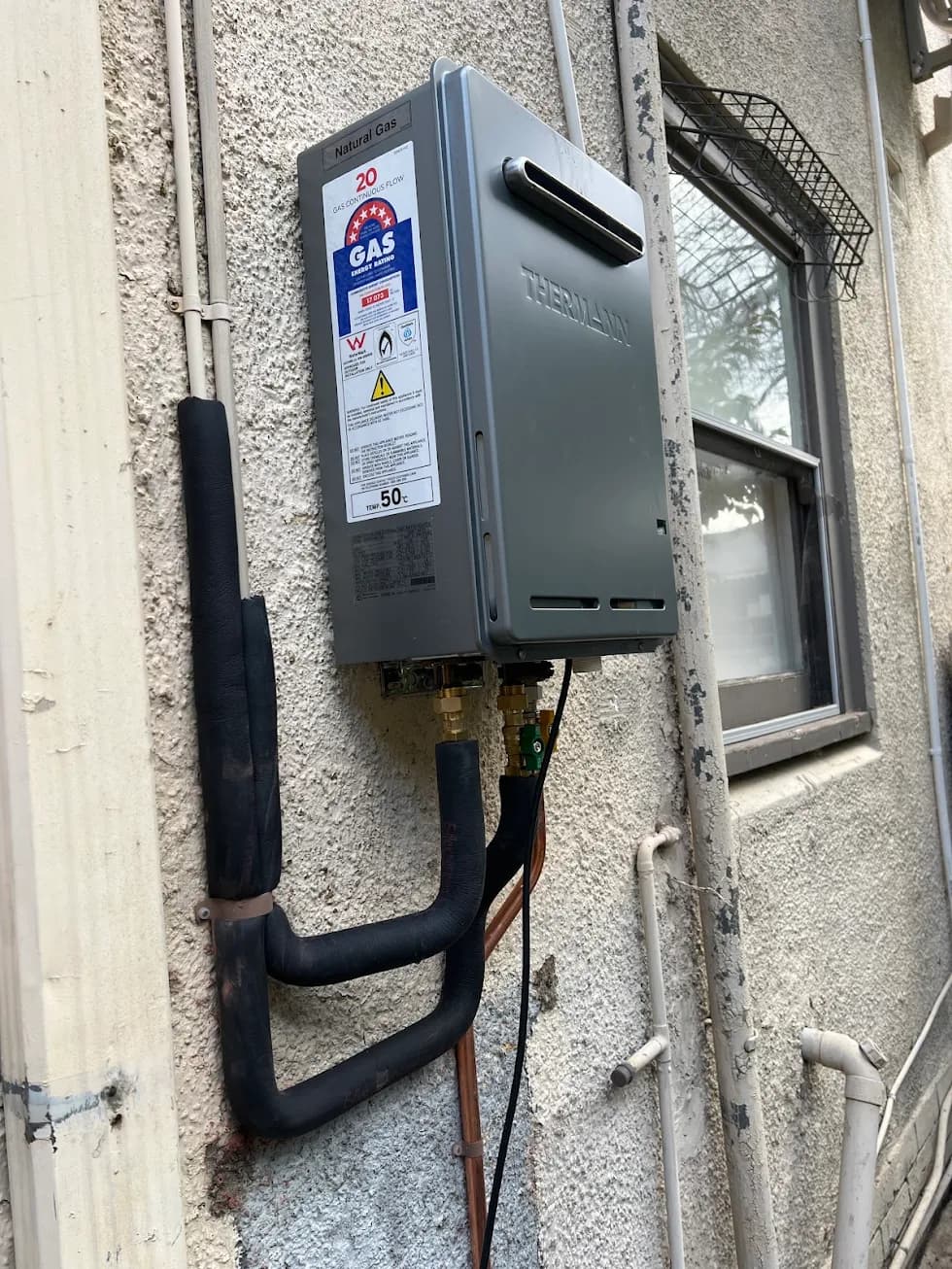 Wall-mounted Thermann natural gas hot water unit with insulated pipework on an external wall