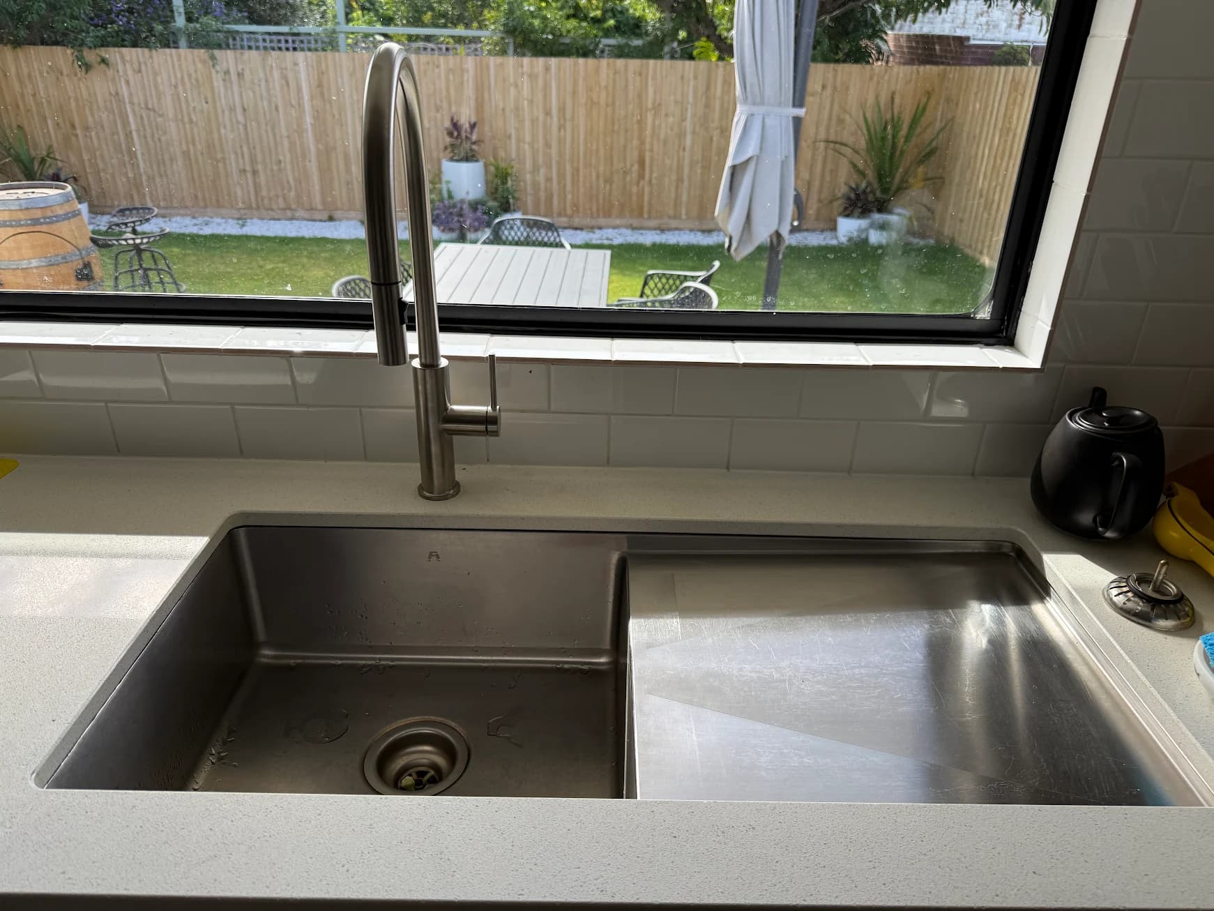 Double-bowl stainless steel kitchen sink with a tall mixer tap beneath a large window