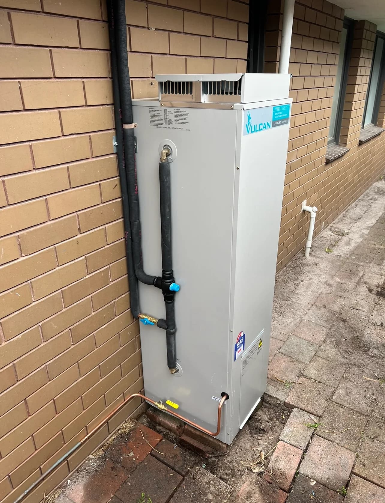 Vulcan outdoor hot water system with insulated pipework and copper connections against a brick wall