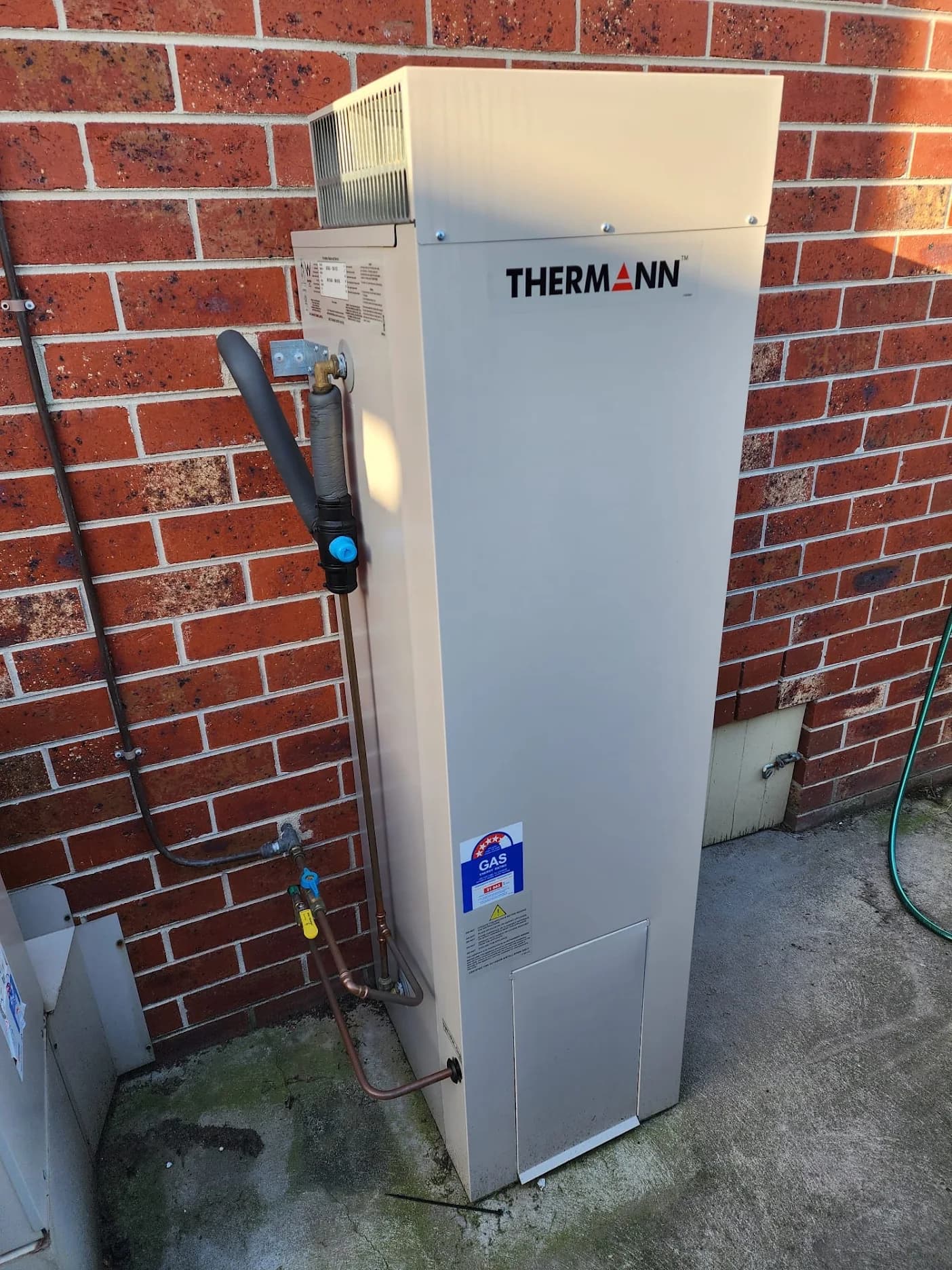 Thermann external hot water system against a red brick wall with insulated pipework