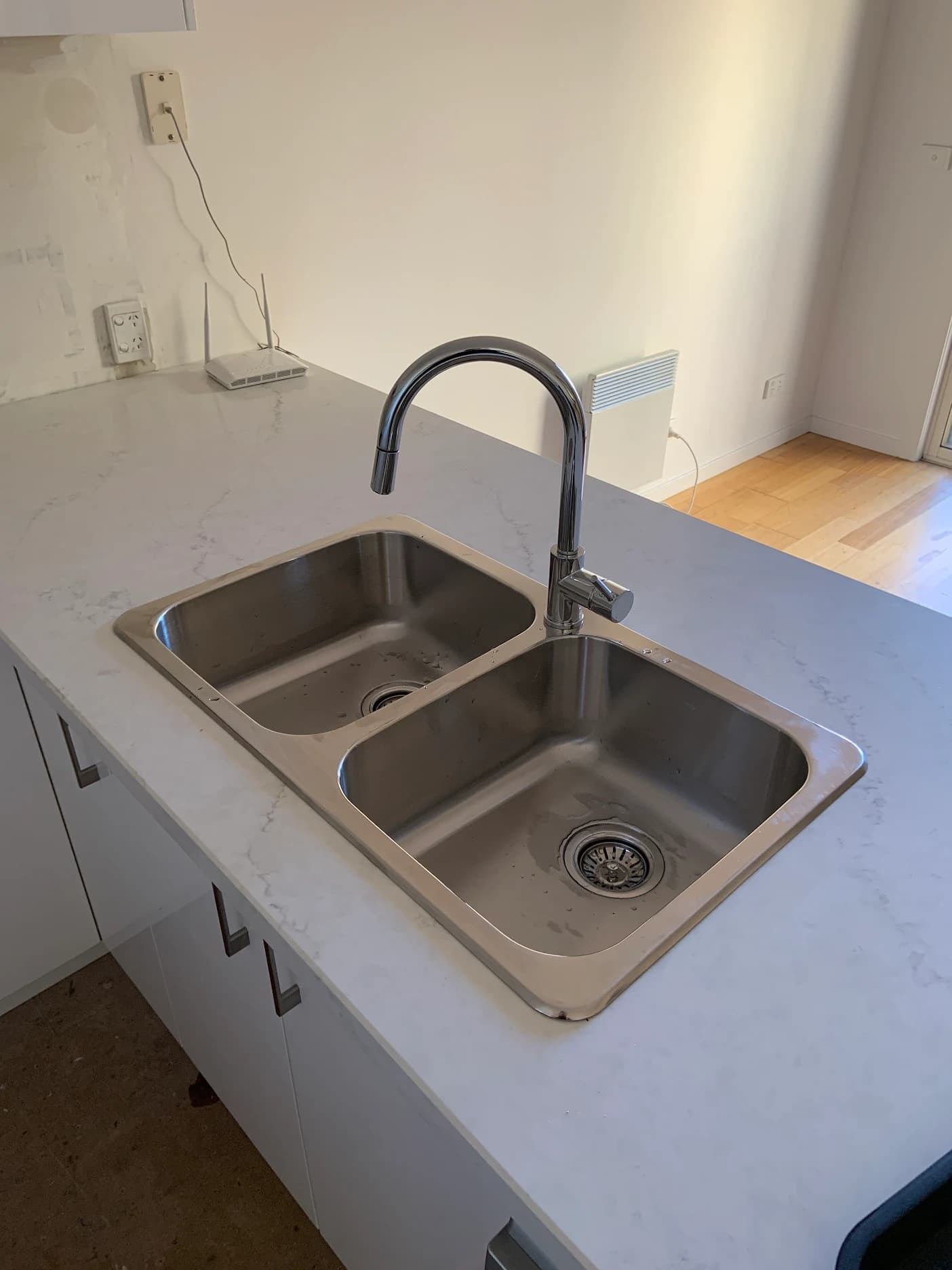 Double-bowl stainless steel kitchen sink with a chrome mixer on a white benchtop